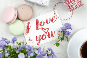 A note that says "I love you" surrounded by cookies, flowers, string, and coffee