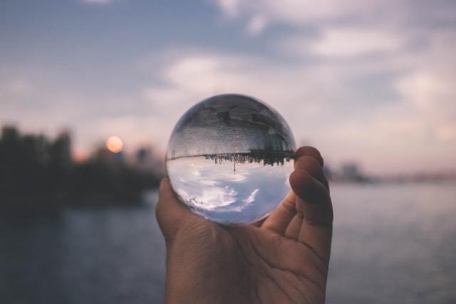 Clouds and a view of a lake reflected upside down in a ball in someone's hand.