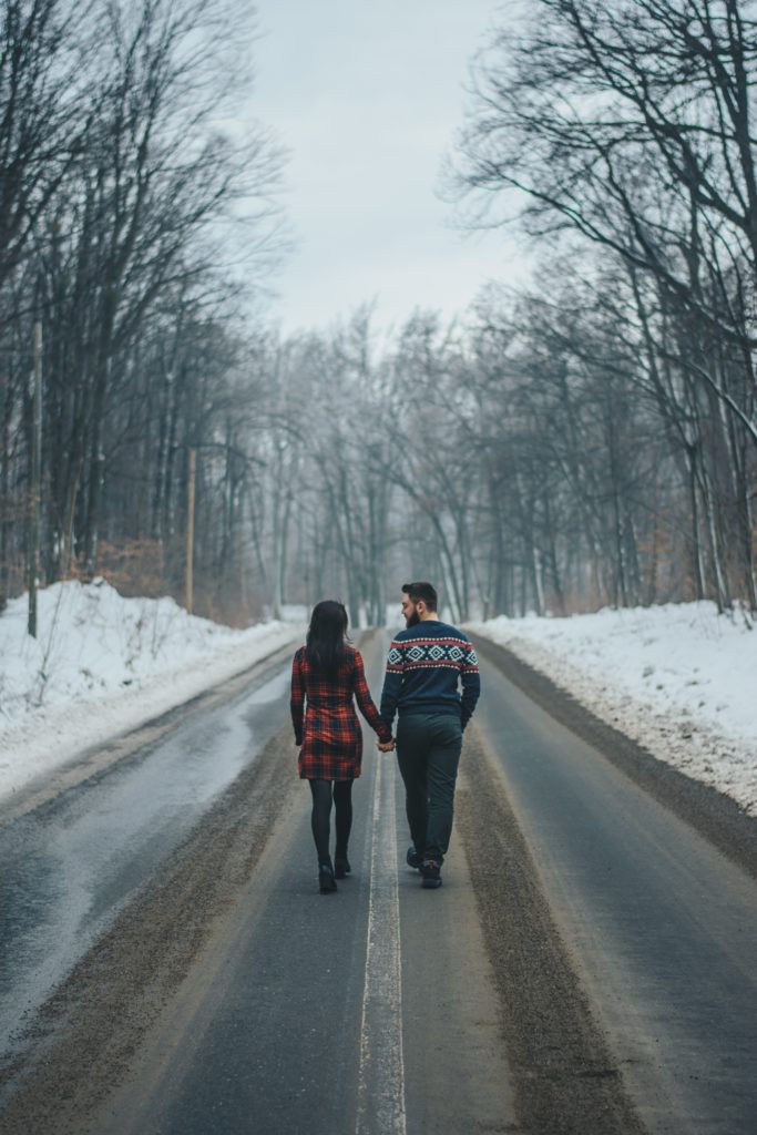 A man and woman holding hands and walking down a snowy road.