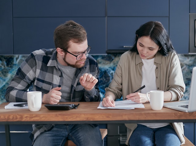 A couple looking together at some papers, probably discussing finances, with a calculator and computer next to them.